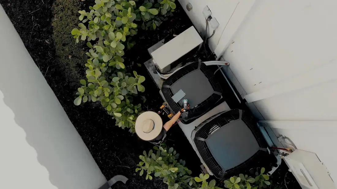 A technician in a straw hat between two new condensers, seen from a drone