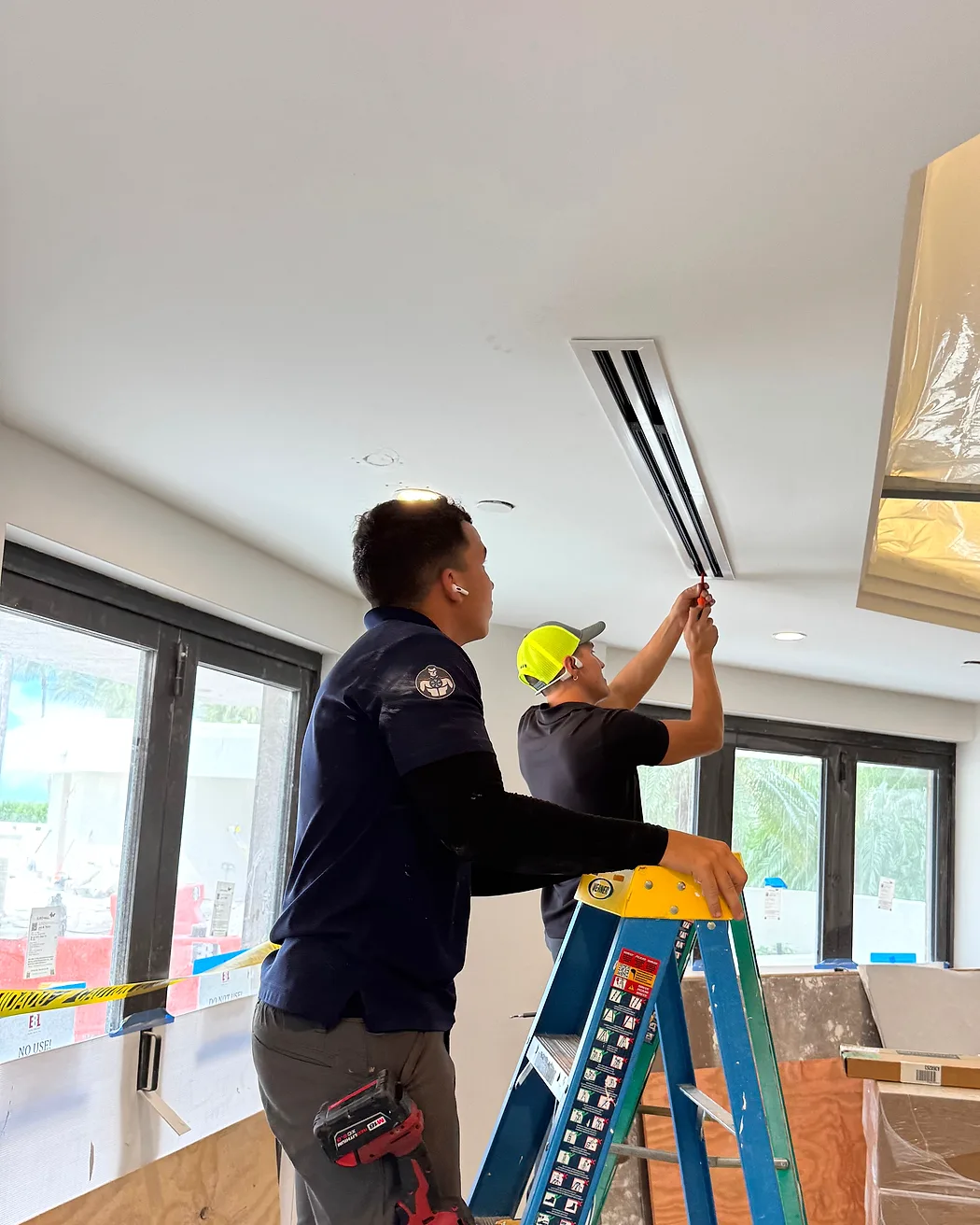 Two ACMAN technicians installing a linear ceiling vent in a new luxury home